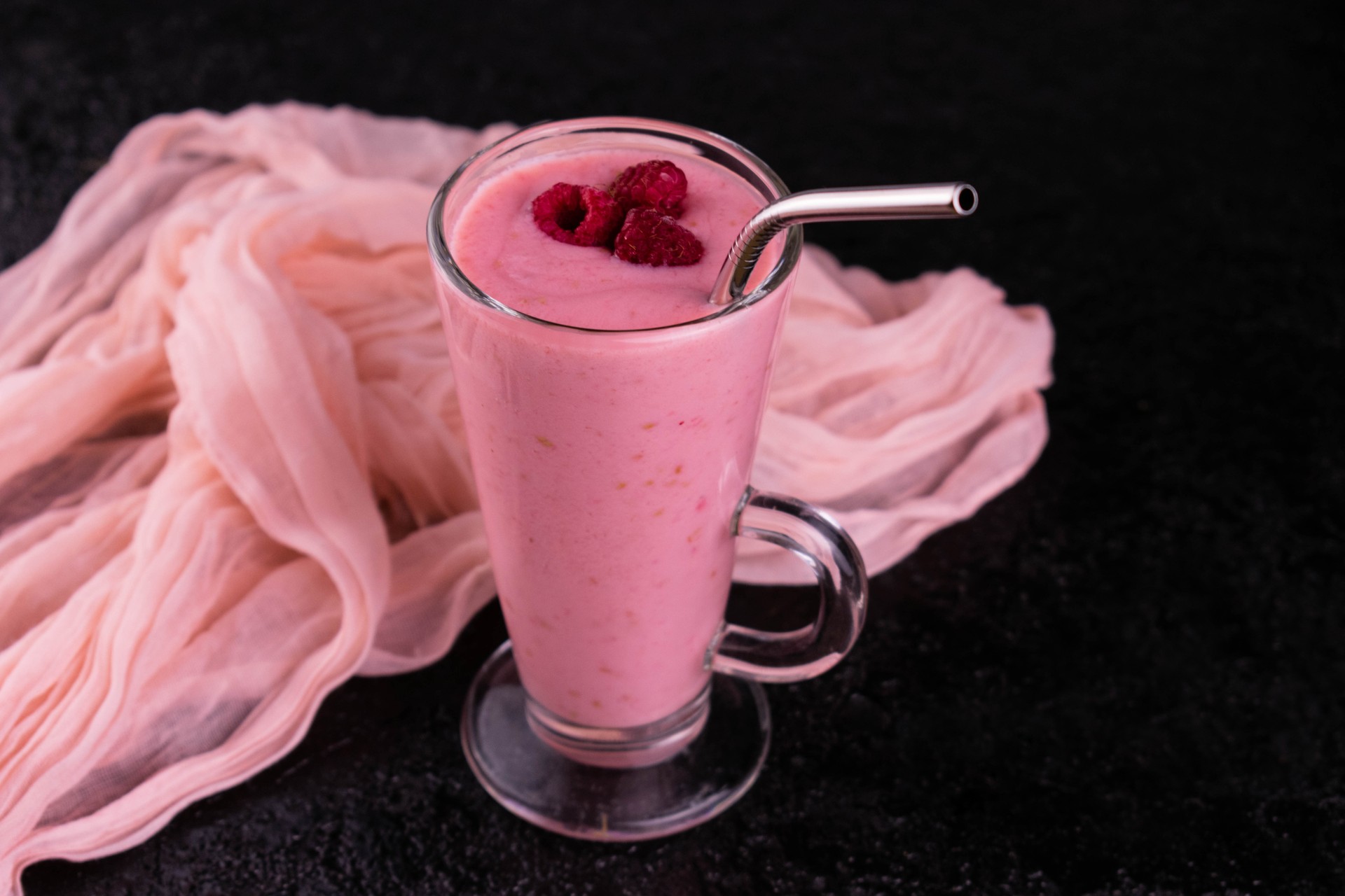 Raspberry smoothie in a tall glass on a black background.