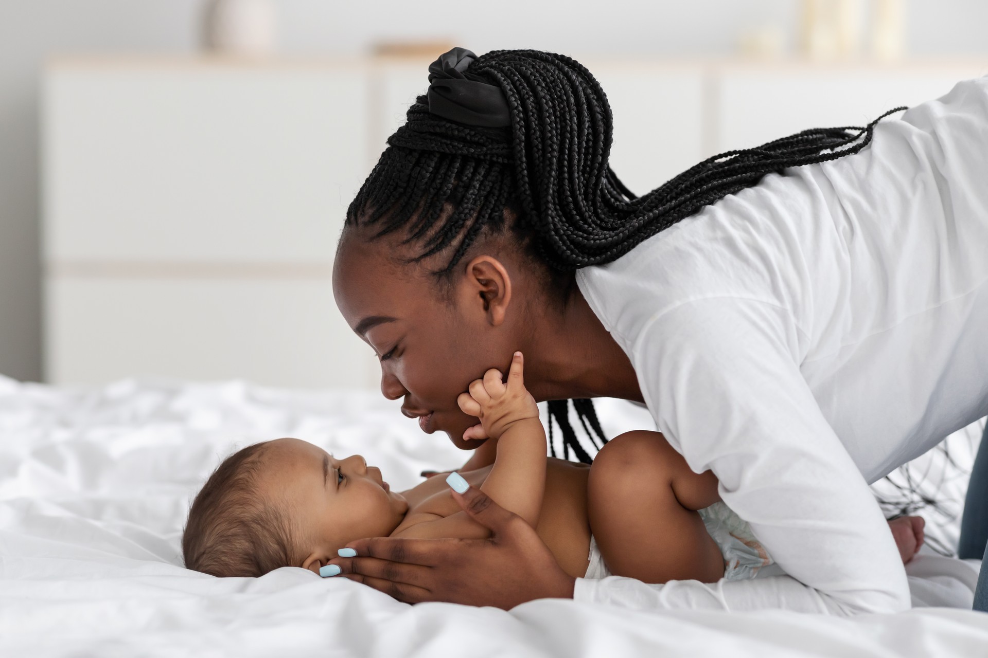 Black mom playing in bed with her infant, kissing baby