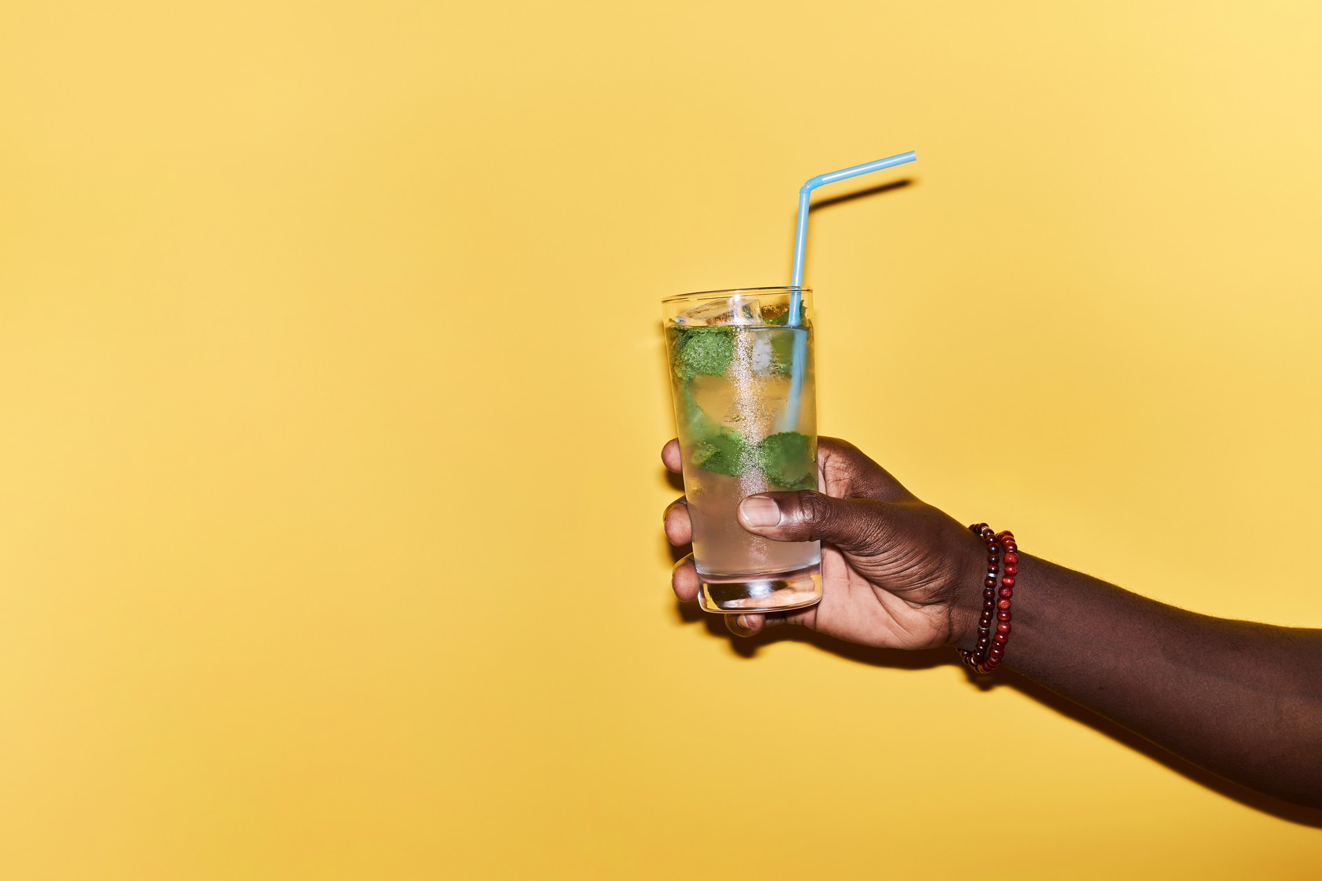 Minimal close up of male hand holding refreshing ice cocktail against yellow