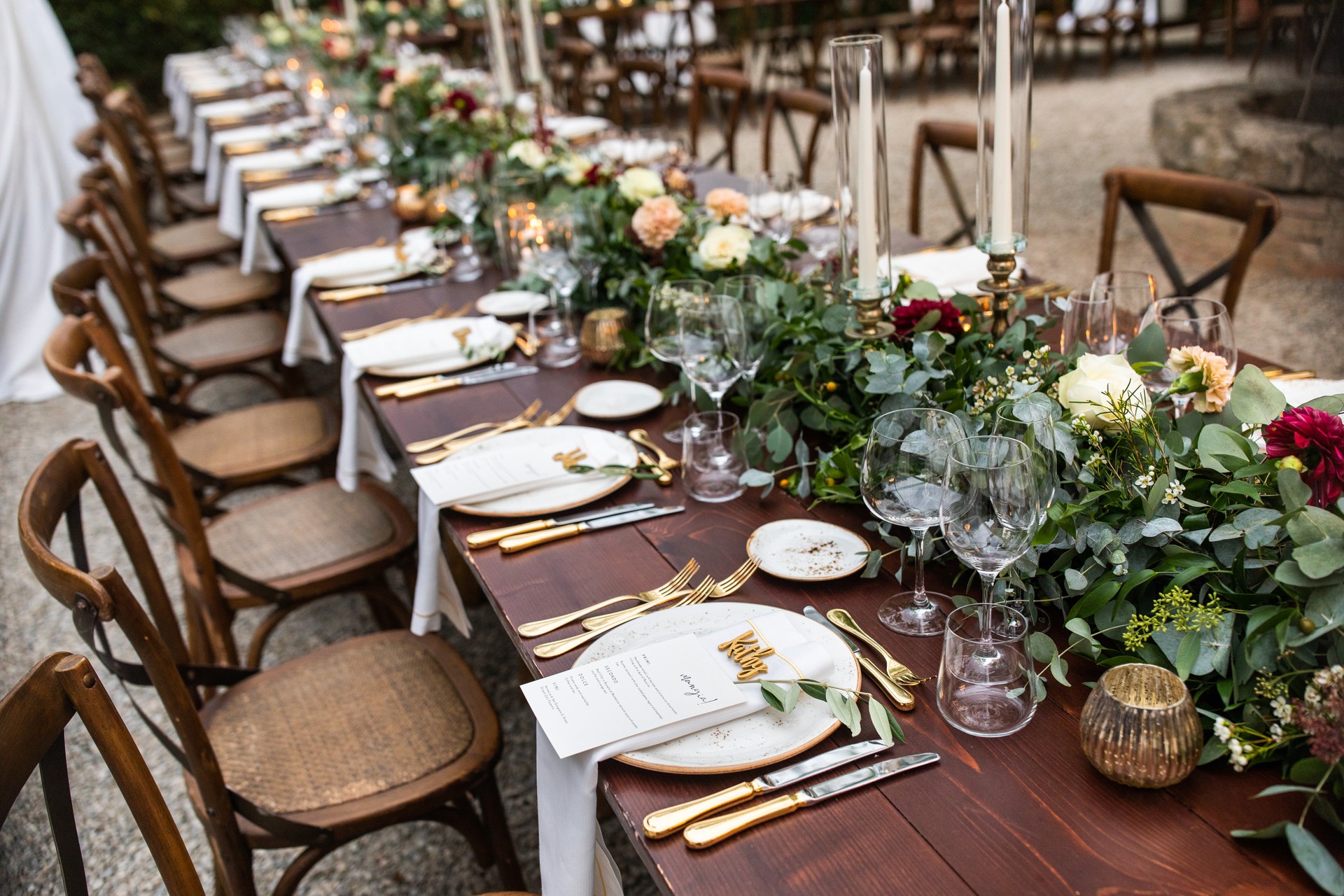 in backyard of villa in Tuscany there is banquet wooden table decorated with cotton and eucalyptus compositions, glasses, candles and plates are placed on table