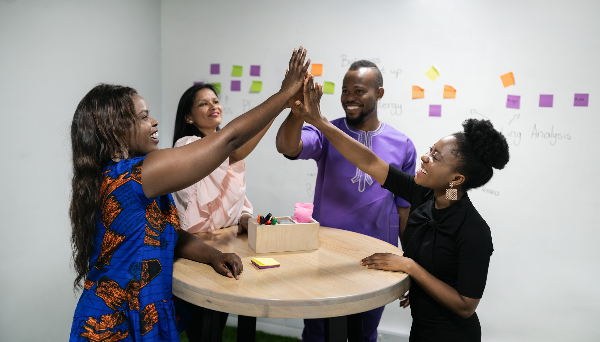 Diverse businesspeople laughing and high-fiving after an office teamwork meeting