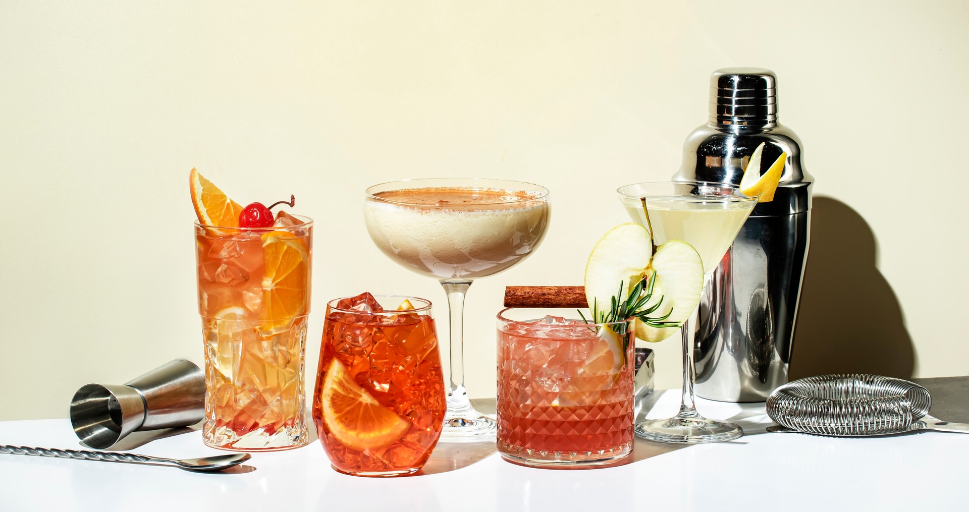 Cocktail party. Bright fruity and citrus alcoholic drinks with gin, vodka, vermouth and juice. Beige background, hard light, shadow pattern. Banner